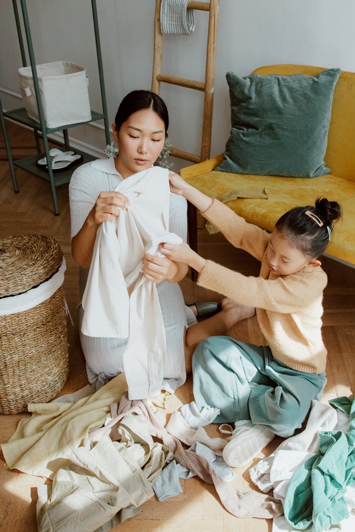 A mother and daughter folding clothes together on the floor in a cozy living room.