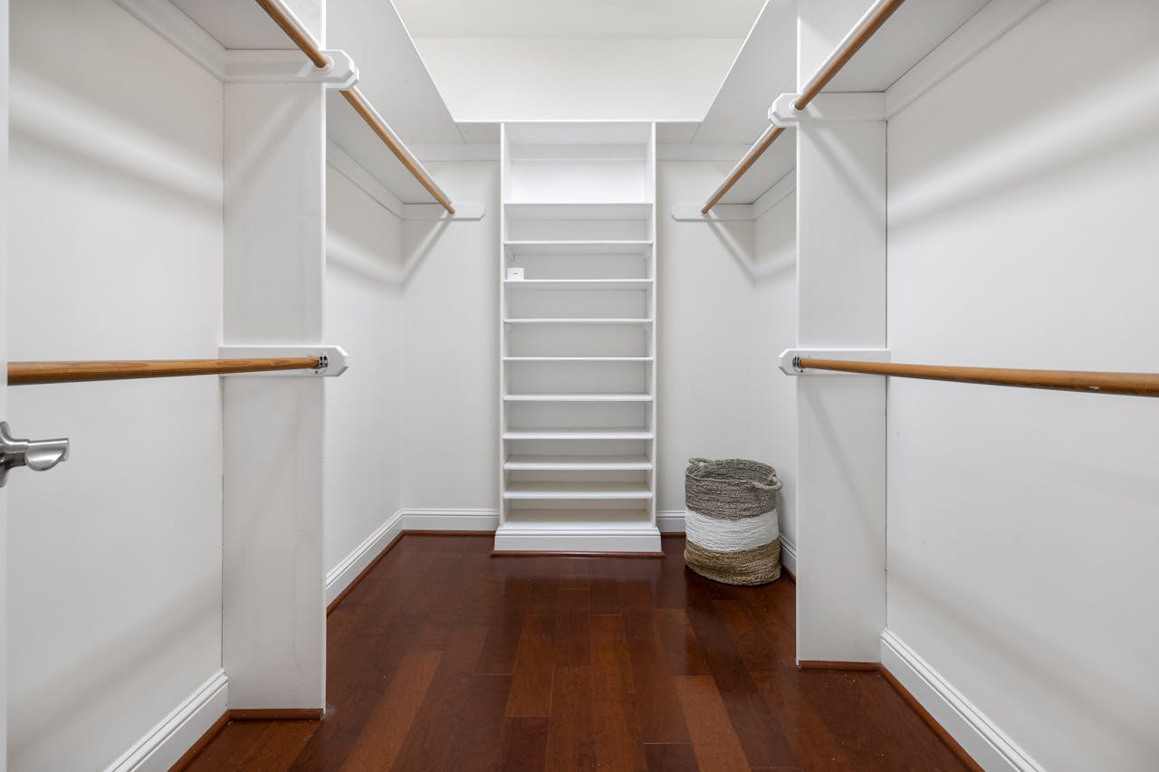 Minimalist empty walk-in closet featuring wooden floors, shelves, and hanging rods.